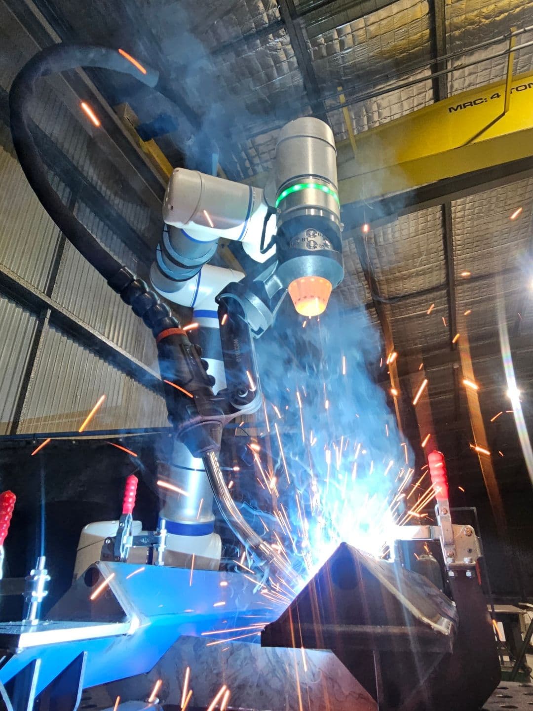 ArcCell cobot welder mid-arc with sparks under overhead gantry