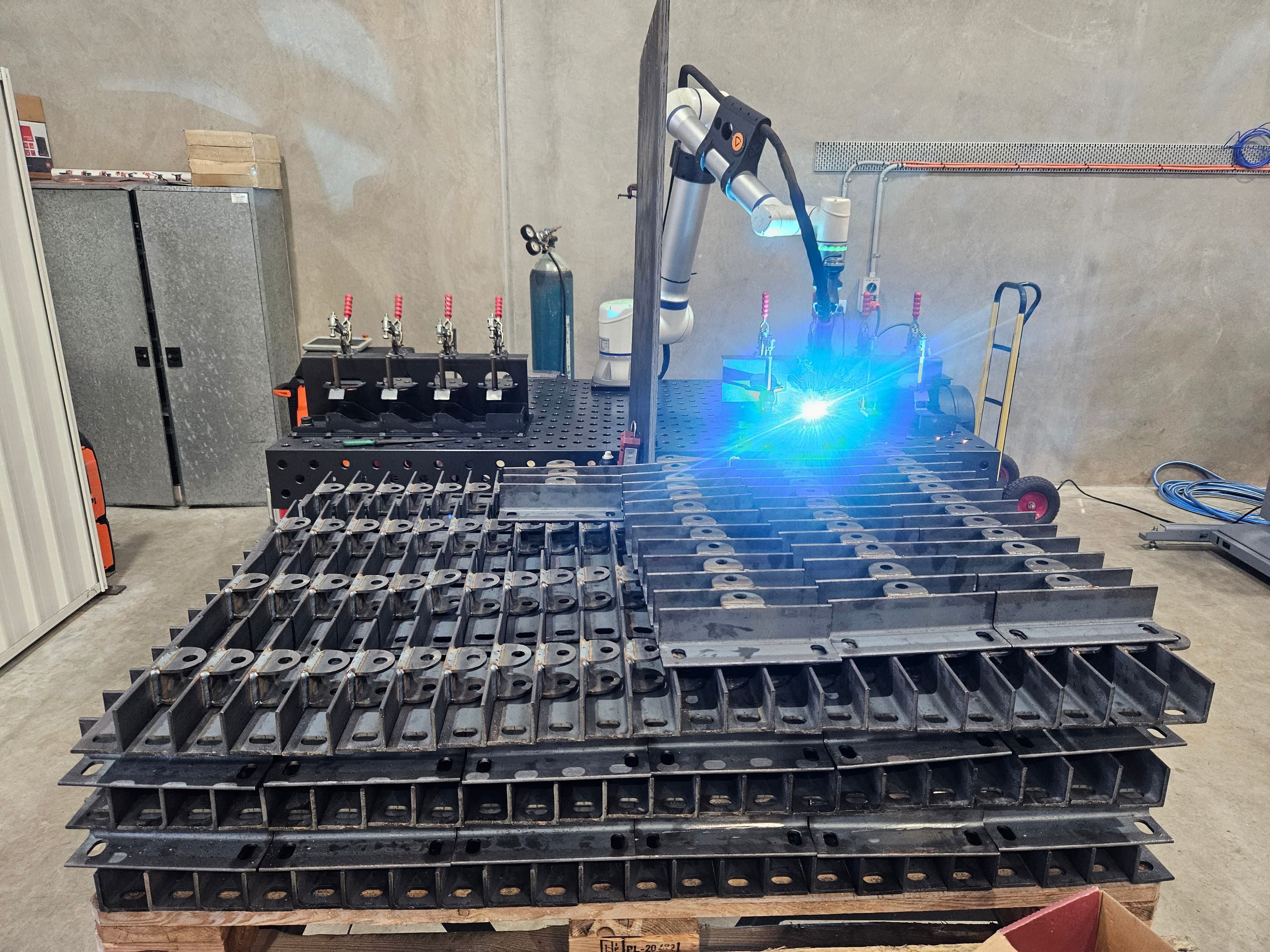 ArcCell mid-arc on a pallet of stacked steel brackets in a factory shed